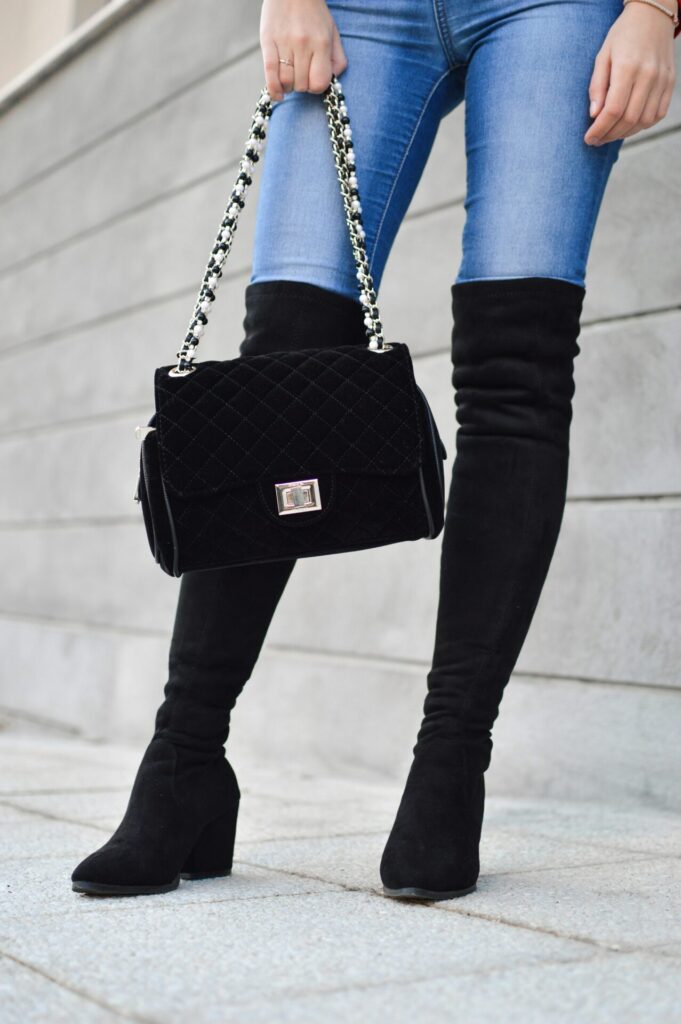 A black handbag held by a lady wearing black boots